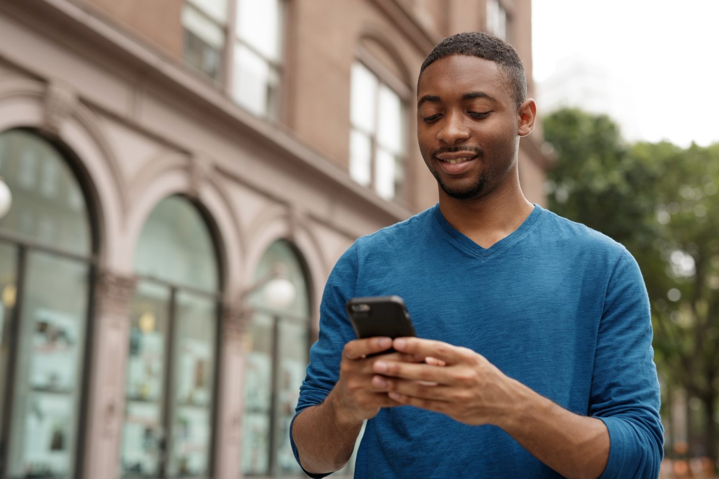 Young african american man walking holding a cell phone checking text messages